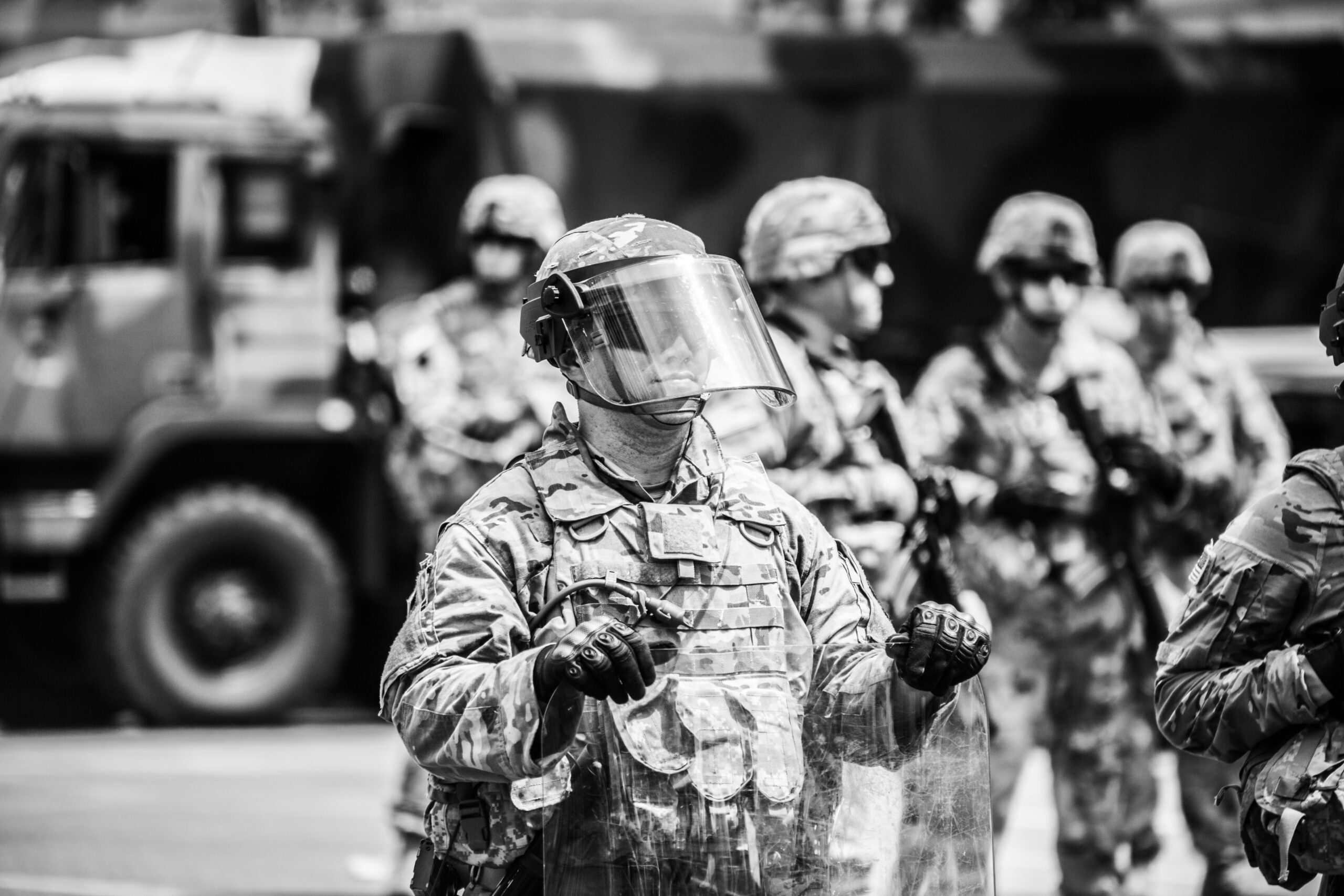 Soldier in riot gear standing with fellow servicemen in the background – symbolising the strength, discipline and hidden emotional toll of life after military service