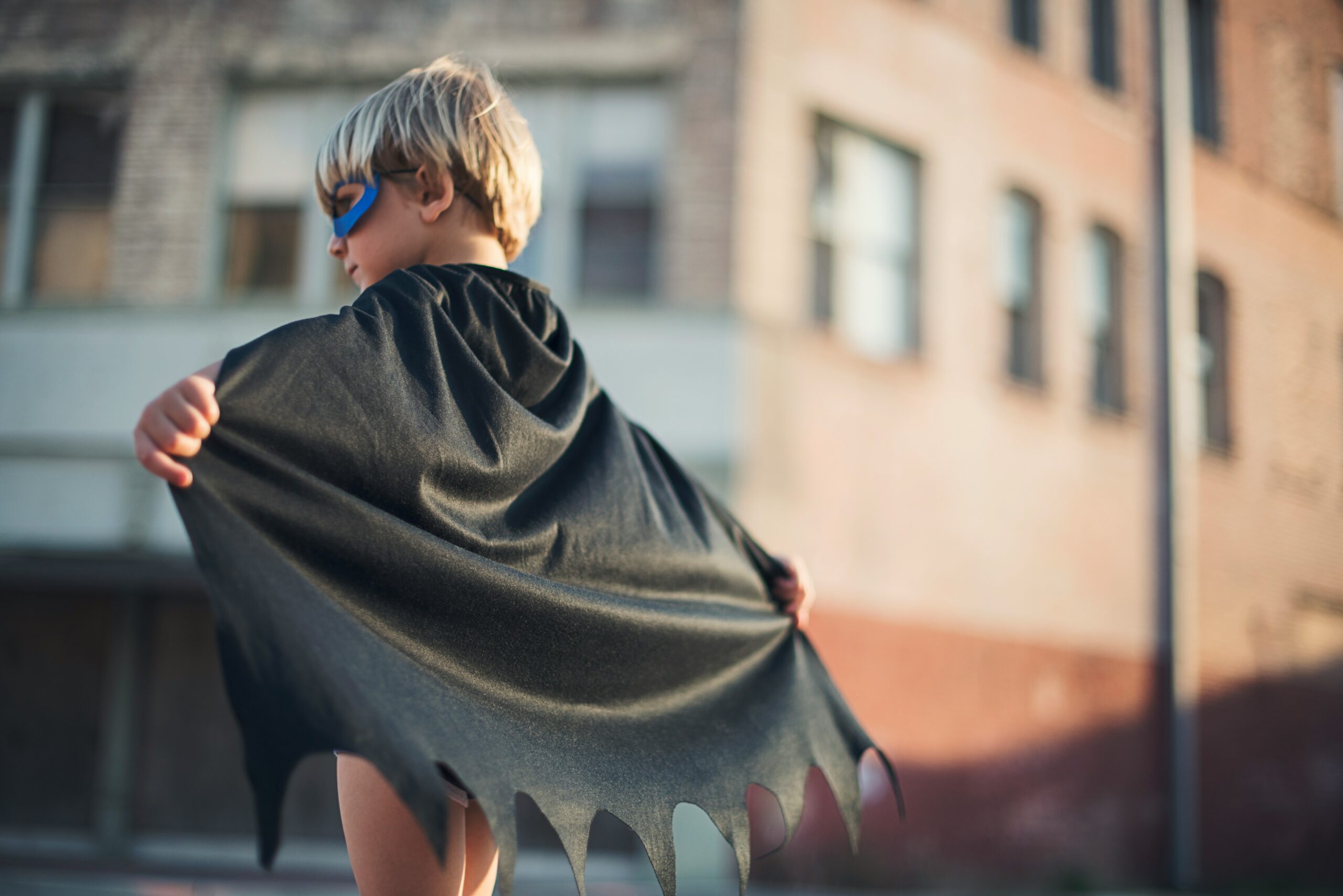 Young boy in a superhero cape and mask standing confidently – representing early gender roles and the pressures on boys to appear strong and fearless