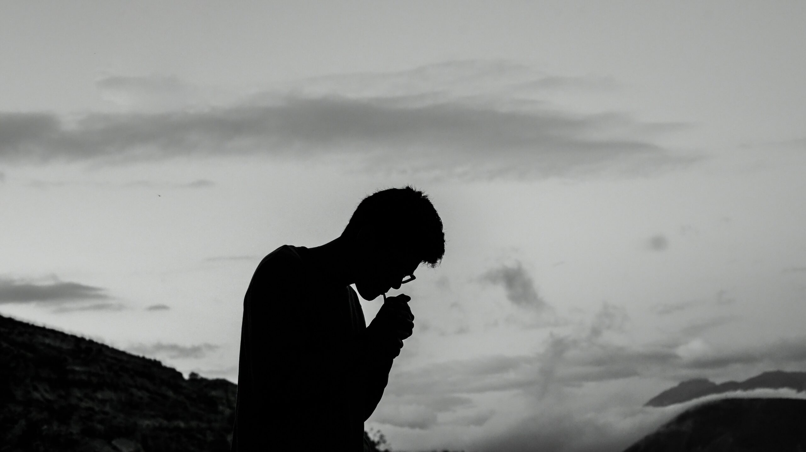 Silhouette of a man in a mountain landscape, head bowed while lighting a cigarette – representing addiction, substance use and emotional struggle in men