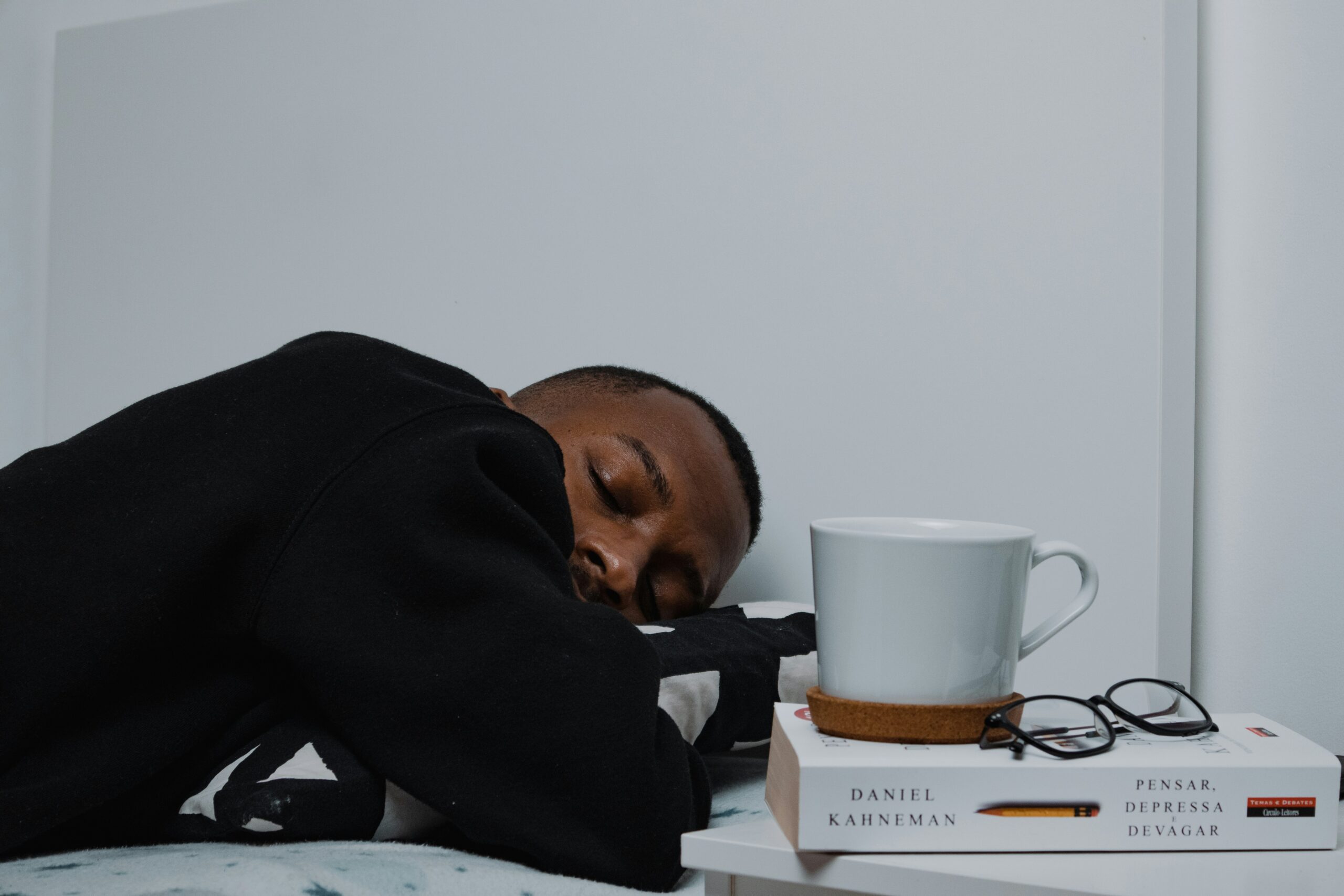 Exhausted man asleep on a bed next to a book, glasses and coffee mug – symbolising burnout, fatigue and mental overload in men