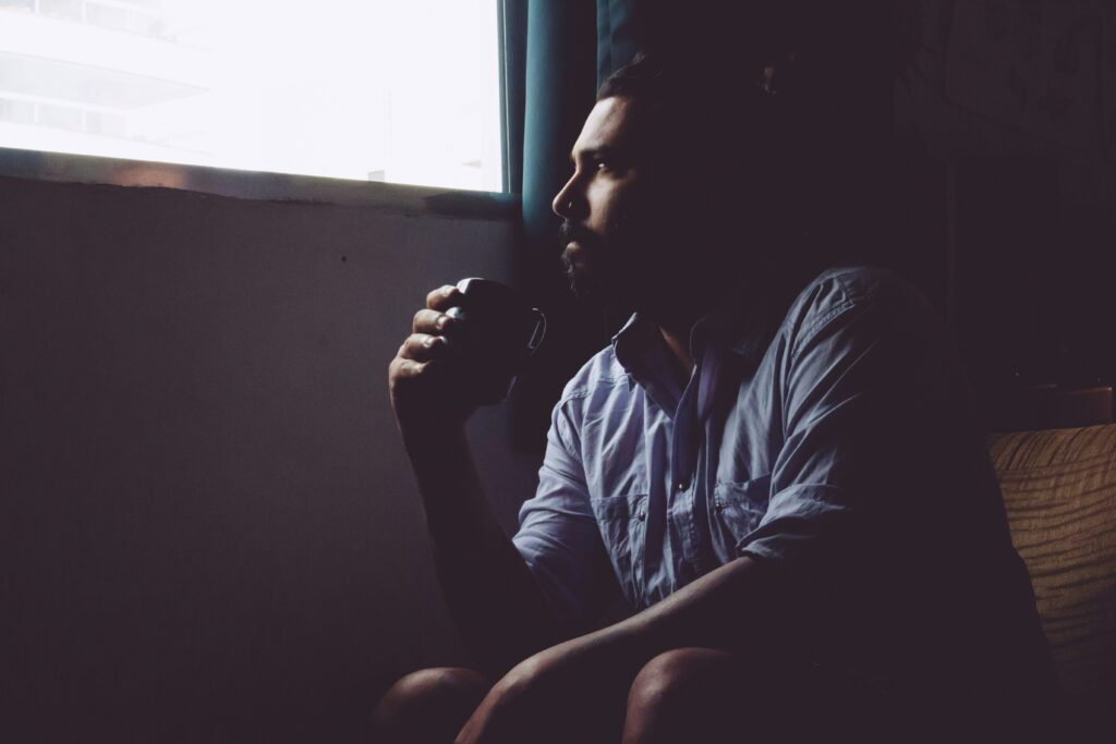 Man sitting quietly with a mug, looking out the window in soft light – reflecting the uncertainty and introspection many feel when starting therapy