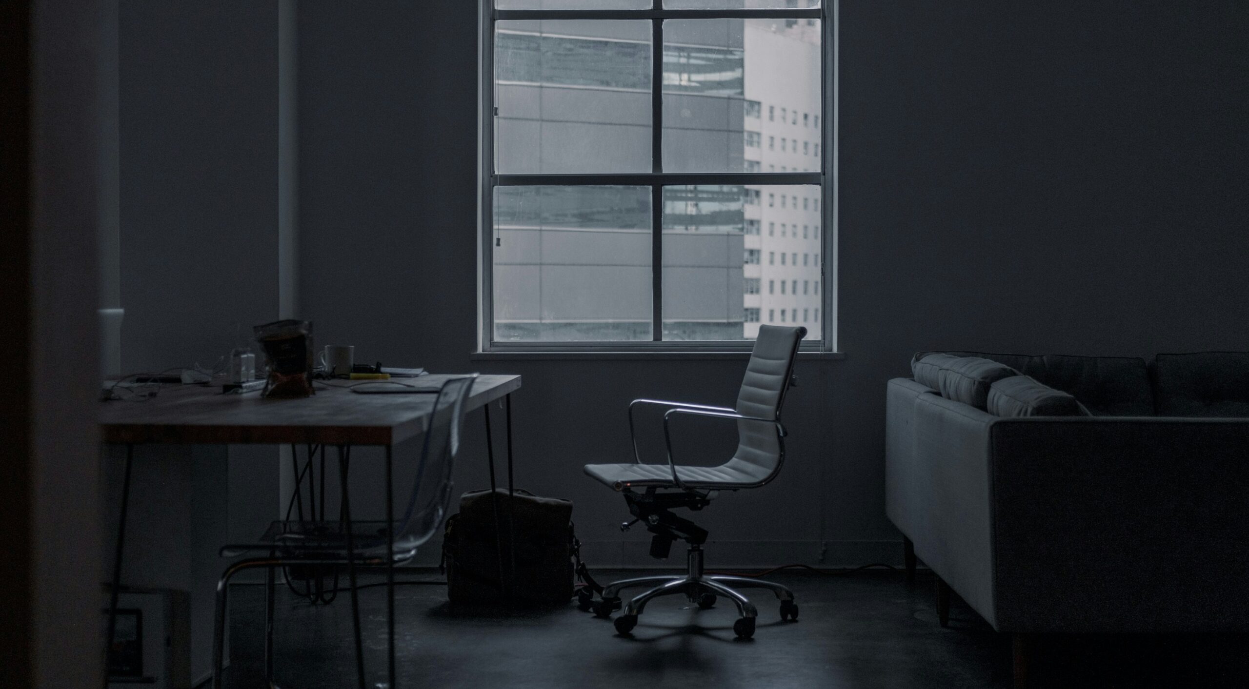 Dimly lit empty office with a desk, chair and city view – representing isolation, stress and mental health challenges in the modern workplace