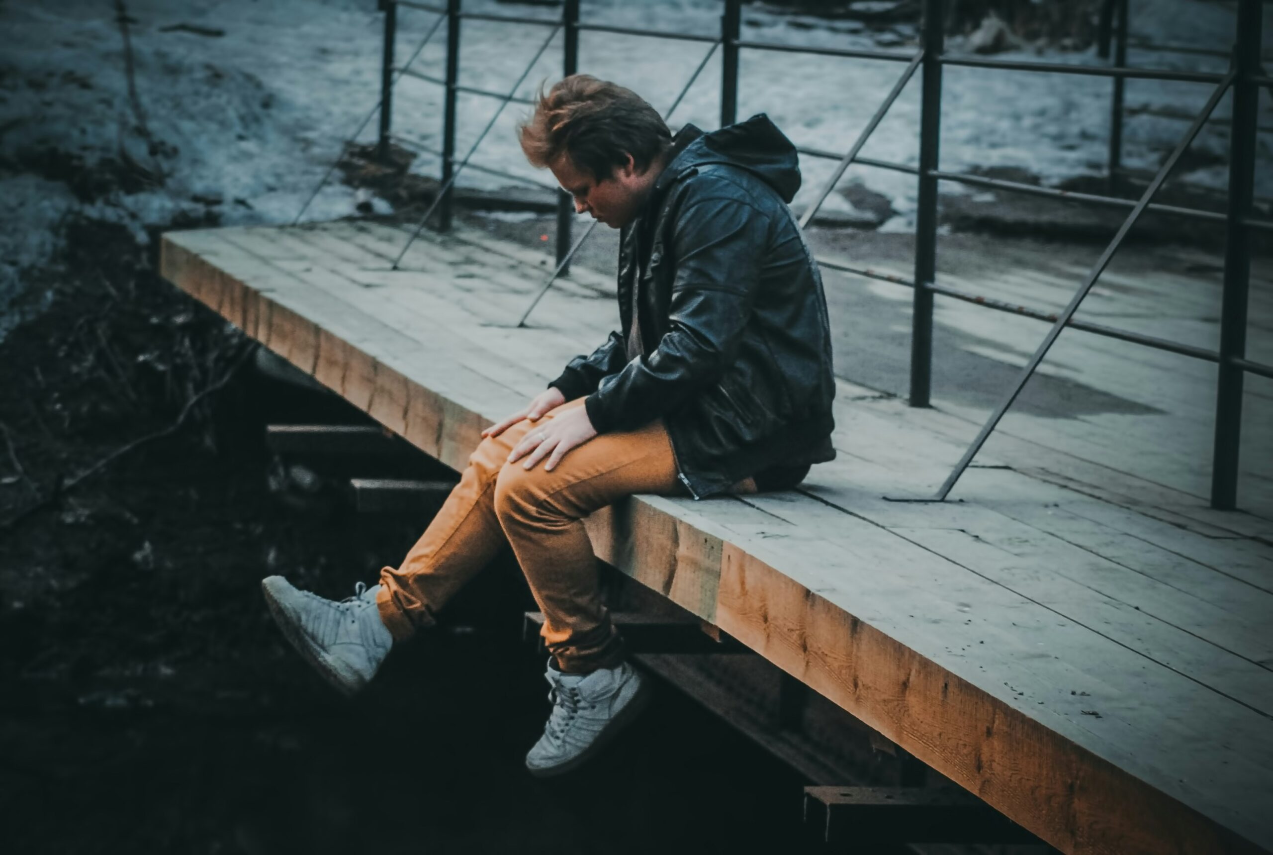 Man sitting alone on a wooden bridge, head down in thought – representing low self-esteem, self-doubt and the emotional weight many men carry in silence