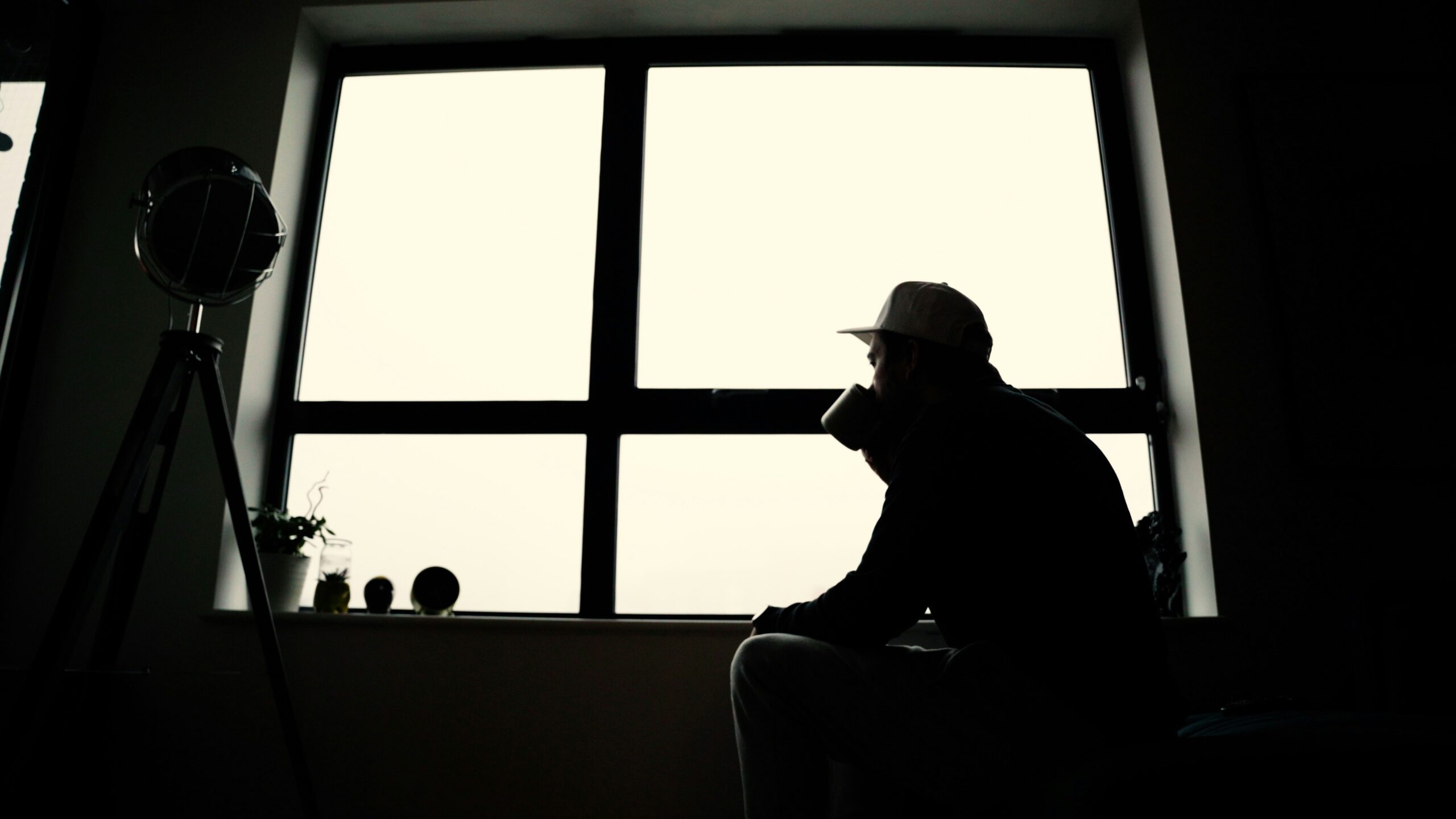 Silhouette of a man in a cap sitting by a window with a mug – reflecting on loss, loneliness and healing after a breakup or divorce