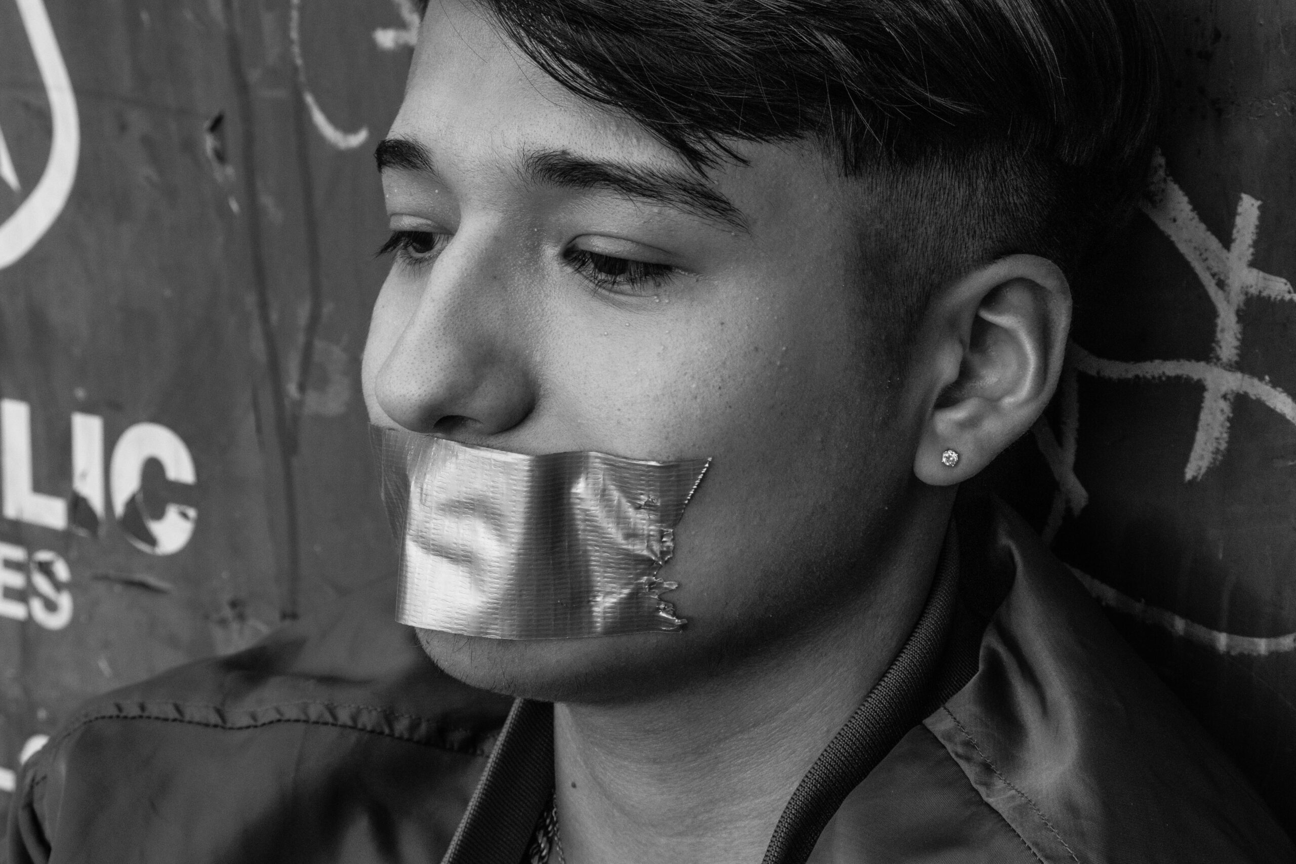 Black and white close-up of a young man with duct tape over his mouth – representing the silencing and stigma surrounding male sexual abuse and assault