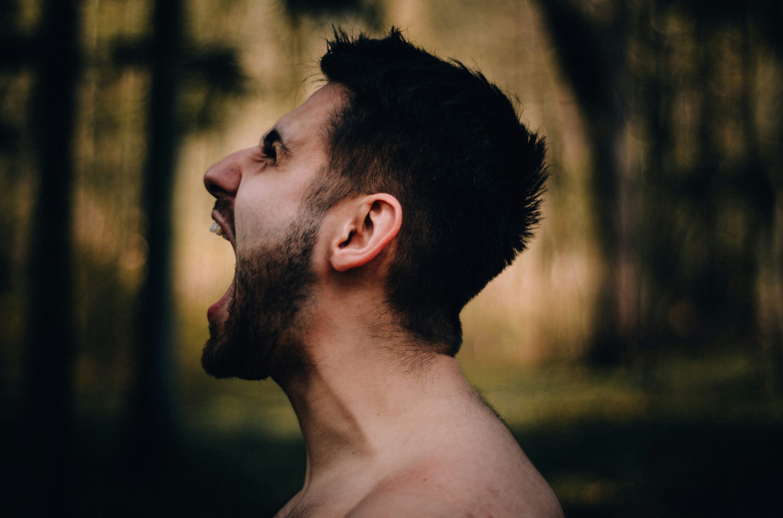 Close-up side profile of a shirtless man shouting in frustration – representing male anger, emotional intensity and the challenge of managing strong feelings