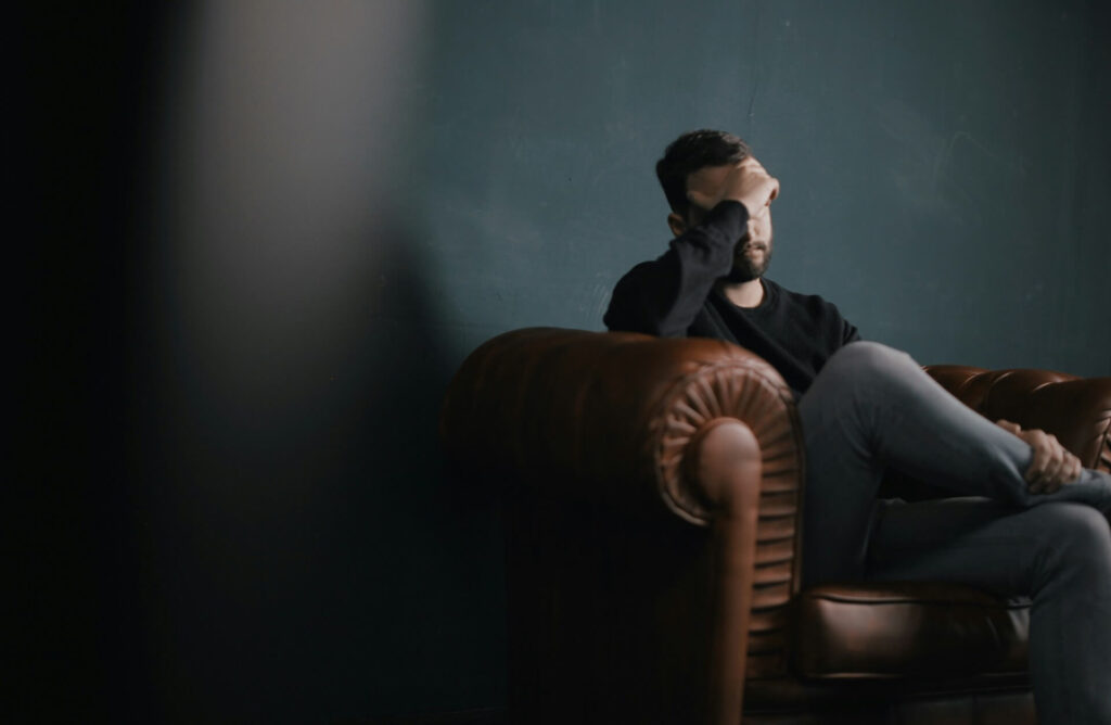 A man sitting on a therapy couch with his head in his hands, expressing his emotions